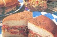 Muffaletta cut in half on plate with black olives.